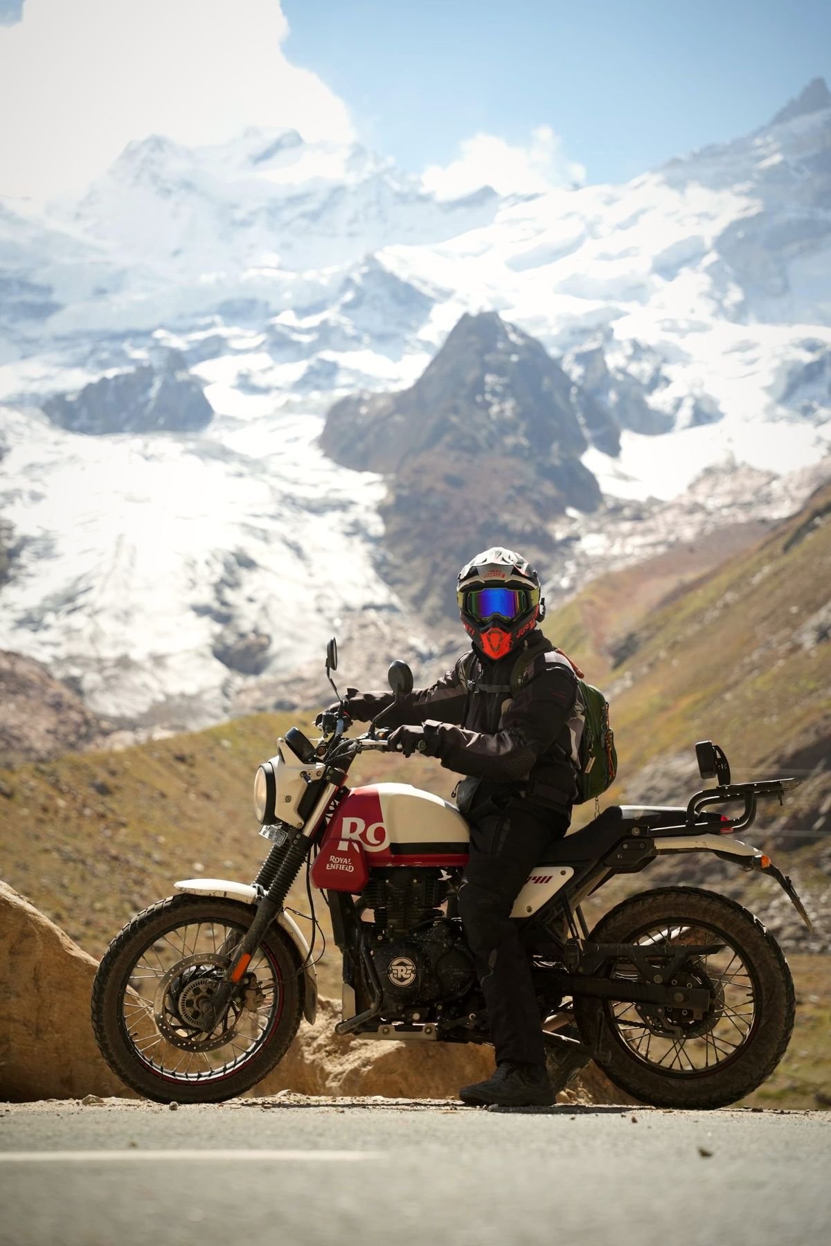 Rider on a Royal Enfield Himalayan in front of a glacier and snow-capped Himalayan peaks