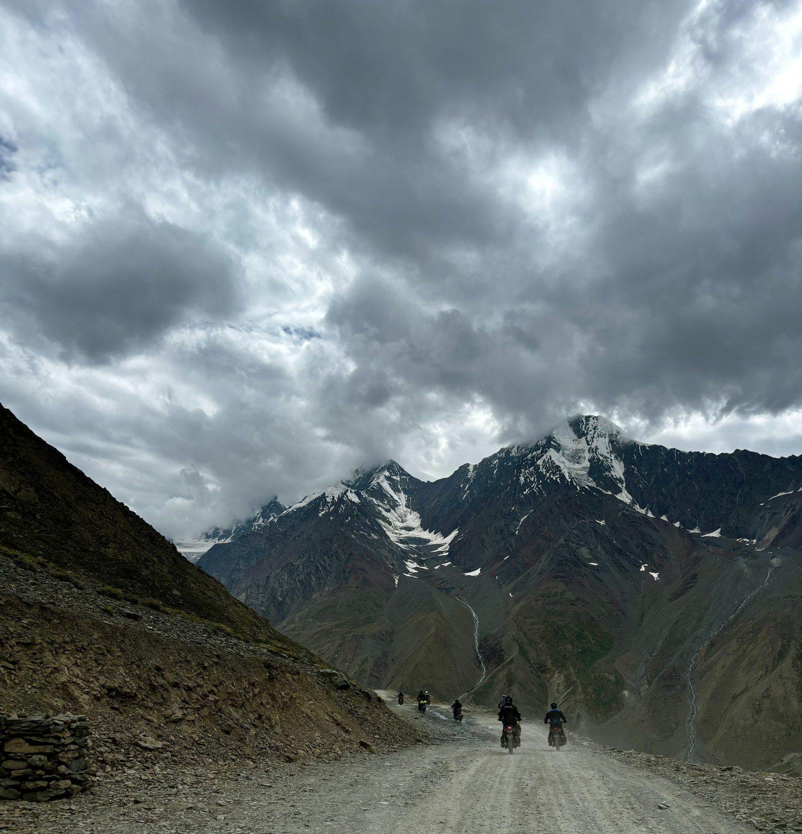 Group of riders on a gravel road below snow-capped Himalayan peaks